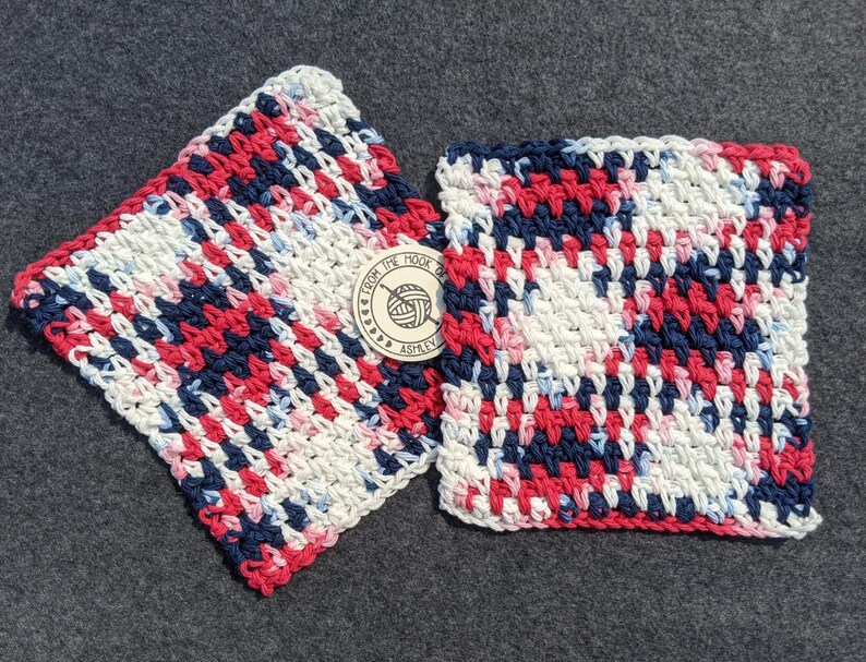 May include: Two square, handmade crochet washcloths. The washcloths are a mix of red, white, and navy blue yarn. A small, round tag with the text "From the Hook of Ashley" is attached to one of the washcloths.