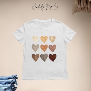 May include: White t-shirt with a design of nine different colored hearts. The hearts are arranged in three rows of three. The text "Kand idly Me Co." is printed at the top of the shirt.