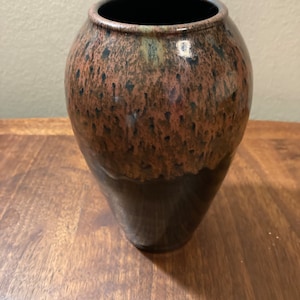 May include: A brown and black ceramic vase with a speckled glaze. The vase has a rounded body and a narrow opening.