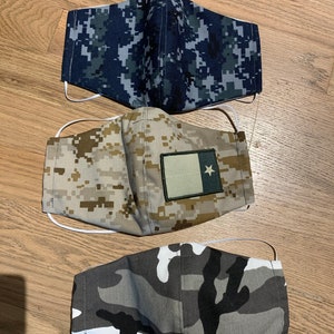 May include: Three different camouflage patterned face masks. The first mask is blue and gray, the second is tan and brown with a small Texas flag patch, and the third is gray, white, and black.