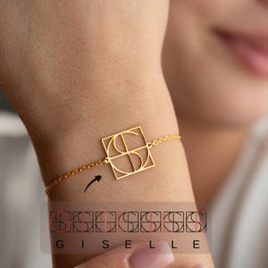 May include: A gold-colored bracelet featuring a square pendant with the letters "GS" inside. The bracelet is attached to a delicate chain. The word "GISELLE" is printed below the bracelet.