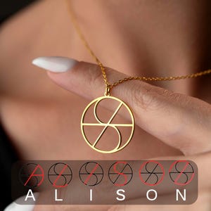 May include: A gold-colored pendant necklace with a circular design. The pendant features a geometric pattern with a stylized letter "S" inside a circle. The necklace is held by a person. The word "ALISON" is displayed below the necklace.