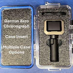 May include: A clear plastic case with a black foam insert. The case contains a black and tan Garmin Xero Chronograph. The case has the text "Garmin Xero Chronograph Case Insert Multiple Case Options" printed on the side.