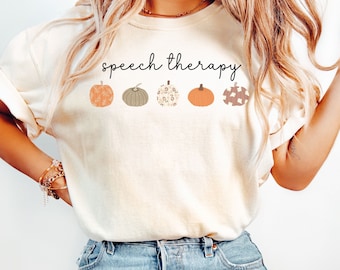 May include: A white t-shirt with the text "speech therapy" and a row of five illustrated pumpkins in fall colors.