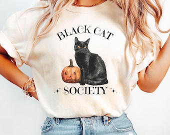 May include: A white t-shirt with the text "Black Cat Society" and a black cat sitting next to a jack-o'-lantern.