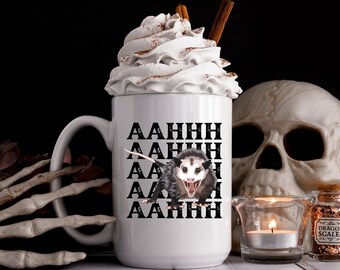 May include: White ceramic mug with a black and white illustration of a possum with the text "AAHHH" repeated five times. The mug is filled with whipped cream and a cinnamon stick.