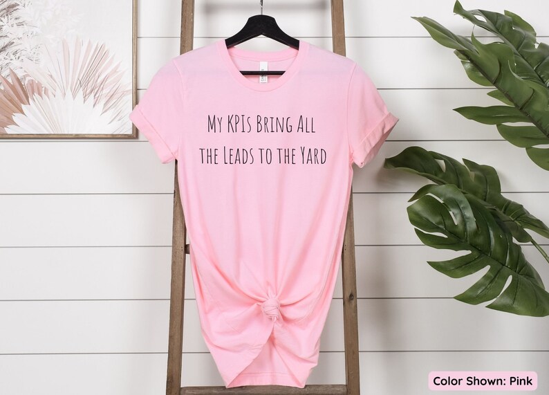 Pu&ograve; includere: Maglietta rosa con la scritta "My KPIs Bring All The Leads To The Yard" stampata sul davanti.