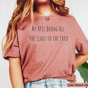 Pu&ograve; includere: Una t-shirt color malva melange con la scritta "My KPIs bring all the leads to the yard" stampata sul davanti.