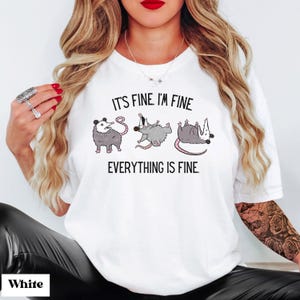 Puede incluir: Camiseta blanca con un gr&aacute;fico de tres zarig&uuml;eyas en diferentes poses. El texto "It's fine. I'm fine. Everything is fine." est&aacute; impreso en la camiseta.
