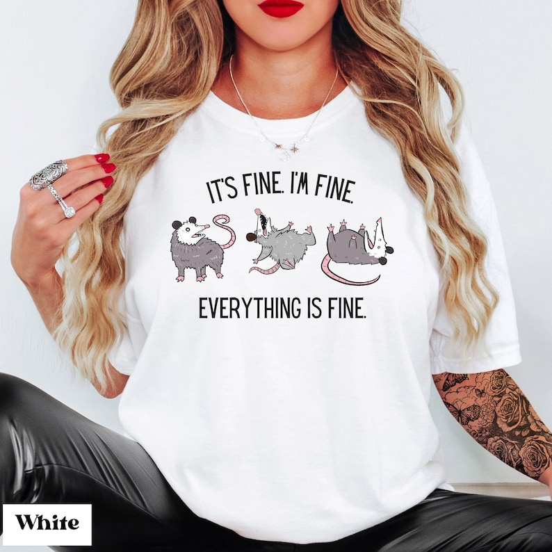 Puede incluir: Camiseta blanca con un gr&aacute;fico de tres zarig&uuml;eyas en diferentes poses. El texto "It's fine. I'm fine. Everything is fine." est&aacute; impreso en la camiseta.