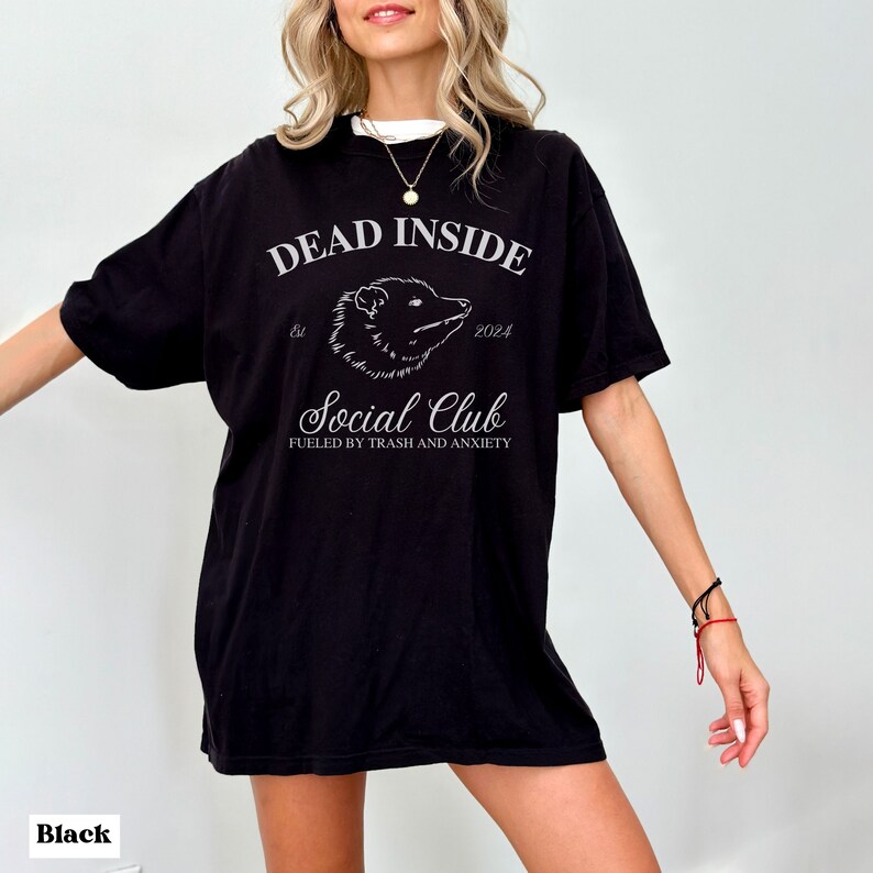 May include: Black oversized t-shirt with a white graphic print that says "Dead Inside Est. 2024 Social Club Fueled by Trash and Anxiety".