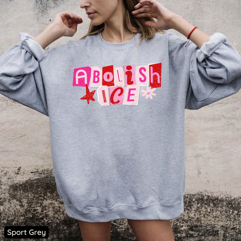 May include: Sport grey sweatshirt with the text "Abolish ICE" in pink and red cut-out letters. A red star and a pink flower accent the text. The sweatshirt has long sleeves.