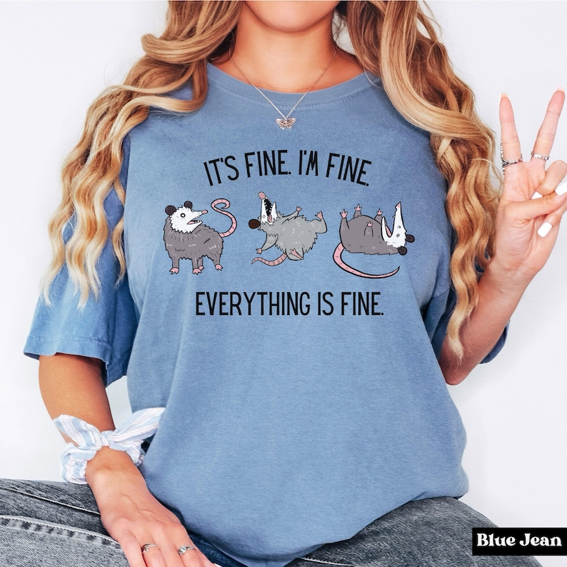 Puede incluir: Una camiseta azul con el texto "It's fine. I'm fine. Everything is fine." y tres zarig&uuml;eyas de dibujos animados.