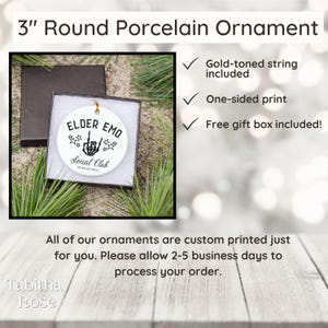 May include: A 3-inch round porcelain ornament with the text "ELDER EMO Social Club" and a skeleton hand illustration. The ornament includes a gold-toned string and a free gift box. The ornament is white with black text and graphics.