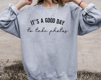May include: A gray sweatshirt with the text "It's a good day to take photos" printed on the front.