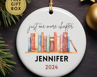 May include: White ceramic ornament with a watercolor illustration of a bookshelf with books. The text "just one more chapter" is written in cursive above the bookshelf. The text "JENNIFER 2024" is written below the bookshelf.