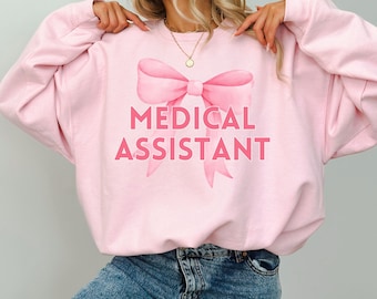 May include: Light pink sweatshirt with a pink bow and the text "MEDICAL ASSISTANT" printed on the front.