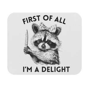 May include: A black and white illustration of a raccoon holding a knife. The raccoon is wearing a bow and the text "First of all I'm a delight" is written below the image.