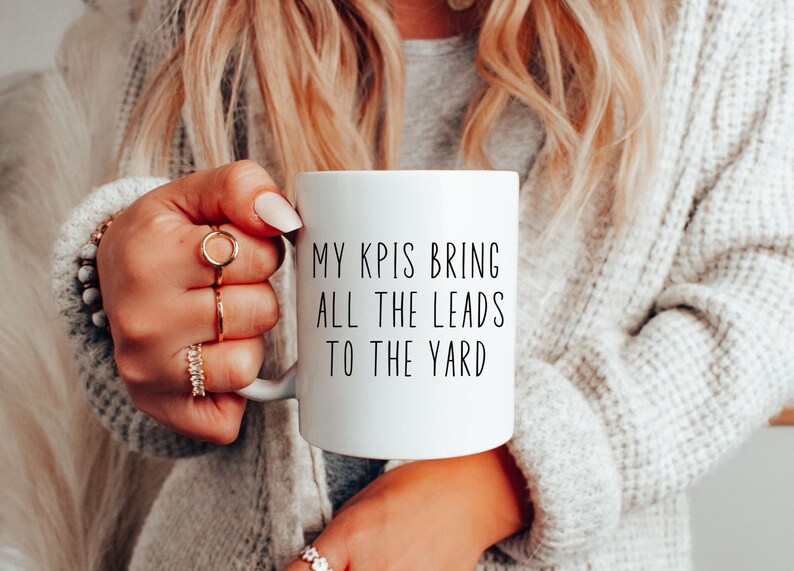 May include: White ceramic coffee mug with black text that reads "My KPIs bring all the leads to the yard".
