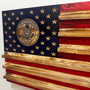 May include: Wooden American flag with the United States Army emblem. The flag features a blue field with gold stars and a gold emblem, and red and natural wood stripes. The flag is made of layered wood.