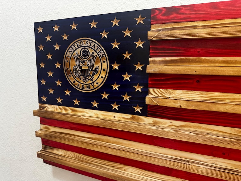 May include: Wooden American flag with the United States Army emblem. The flag features a blue field with gold stars and a gold emblem, and red and natural wood stripes. The flag is made of layered wood.
