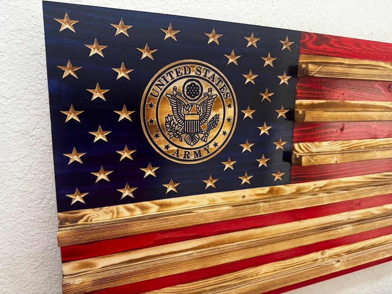 May include: Wooden American flag with the United States Army emblem. The flag features a blue field with gold stars and a gold emblem, and red and natural wood stripes. The flag is made of wooden planks.
