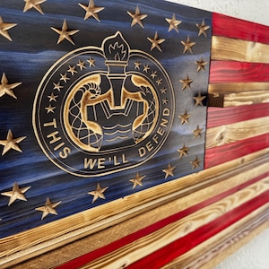 May include: Wooden American flag with carved stars and a circular emblem. The flag features red and white stripes, a blue field with stars, and the text "THIS WE'LL DEFEND".
