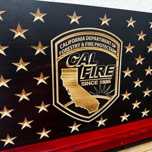 May include: Wooden American flag with carved stars and a red stripe. The flag features the California Department of Forestry & Fire Protection logo, with the text "CAL FIRE SINCE 1885".