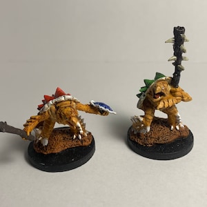 May include: Two painted miniature figures of turtles with spiky shells, one holding a club and the other holding a shield. The turtles are painted in shades of brown, green, red, and white.