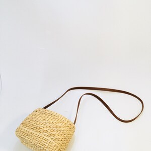 Puede incluir: Un peque&ntilde;o bolso rectangular de paja con una correa de cuero marr&oacute;n. El bolso est&aacute; tejido con paja natural y tiene un dise&ntilde;o simple y cl&aacute;sico.