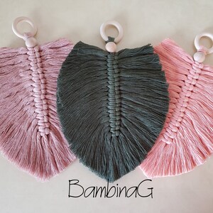 May include: Three macrame leaf decorations in shades of pink and green, each with a wooden ring at the top. The leaves are intricately knotted, creating a textured surface. The text "BambinaG" is visible.