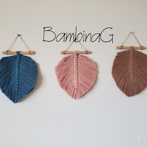 May include: Three macrame feather wall hangings in shades of blue, pink, and brown. Each feather is suspended from a bamboo rod with a natural cord. The text "BambinaG" is written above the feathers.