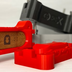 May include: A red 3D printed fingerboard with a wooden deck and a black and gray 3D printed fingerboard in the background.