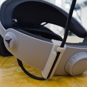May include: A white and black virtual reality headset with a black cable attached to the side. The headset has a white knob on the side for adjusting the fit.