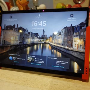 Könnte beinhalten: Ein Tablet mit einem Bildschirm, der eine Stadtlandschaft mit einem Kanal zeigt, flankiert von blauen und gelben Gamecontrollern. Auf dem Bildschirm ist die Uhrzeit 16:45 zu sehen. Die Controller sind an einem roten Rahmen befestigt.