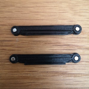 Puede incluir: Dos piezas de plástico negro con una superficie texturizada y un círculo de metal plateado en cada extremo. Las piezas están sobre una superficie de madera.