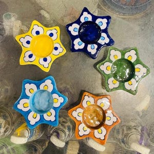 May include: Five star-shaped ceramic bowls arranged in a circle. Each bowl features a central solid color—yellow, dark blue, green, light blue, and orange—surrounded by a white and blue floral-inspired petal pattern along the outer edges.
