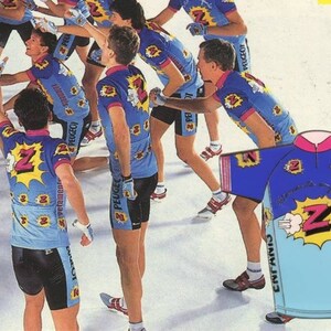 May include: A group of cyclists wearing blue and white cycling jerseys with a large yellow "Z" and the word "Peugeot" on the front. The jerseys have a pink collar and pink trim on the sleeves. The cyclists are wearing black shorts and white socks. The jerseys are for sale.