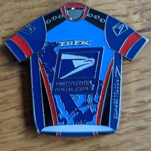 Puede incluir: Un maillot de ciclismo azul y rojo con las palabras "TREK" y "UNITED STATES POSTAL SERVICE" en la parte delantera. El maillot tiene un diseño de águila blanco y azul en la parte delantera.