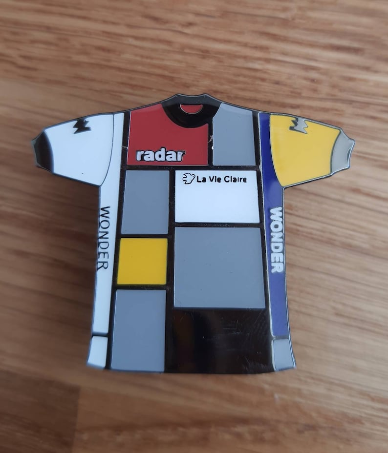 May include: A black and white cycling jersey with a geometric design. The jersey has red, yellow, and blue accents. The text "radar" and "La Vie Claire" are printed on the jersey. The text "WONDER" is printed on the side of the jersey.