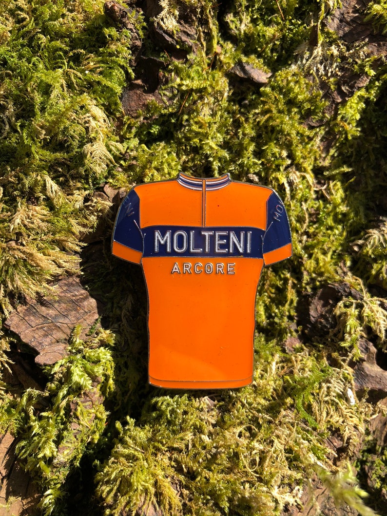May include: Orange and blue cycling jersey enamel pin with the text "MOLTENI ARCORE".