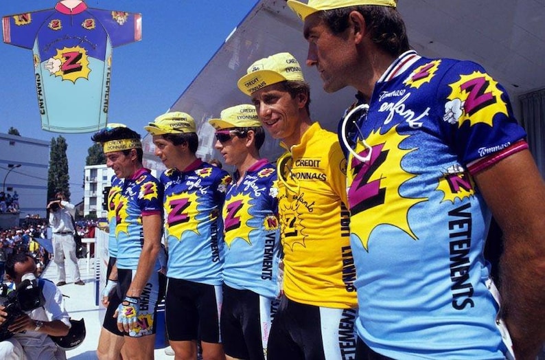 May include: Five cyclists wearing yellow, blue, and black cycling jerseys with a large "Z" logo and the words "Vetements" and "Credit Lyonnais" on the front. The cyclists are wearing yellow caps with the words "Credit Lyonnais" on them.