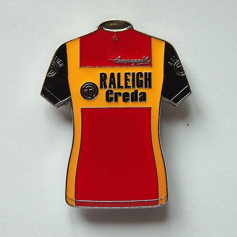 May include: A red, yellow, and black cycling jersey with the text "Raleigh Creda" and a signature on the front.