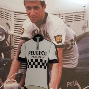 K&ouml;nnte beinhalten: Ein wei&szlig;es Radtrikot mit einem schwarzen Rei&szlig;verschluss und einem schwarz-wei&szlig;en Karomuster. Das Trikot tr&auml;gt den Aufdruck "PEUGEOT MICHELIN" auf der Vorderseite.