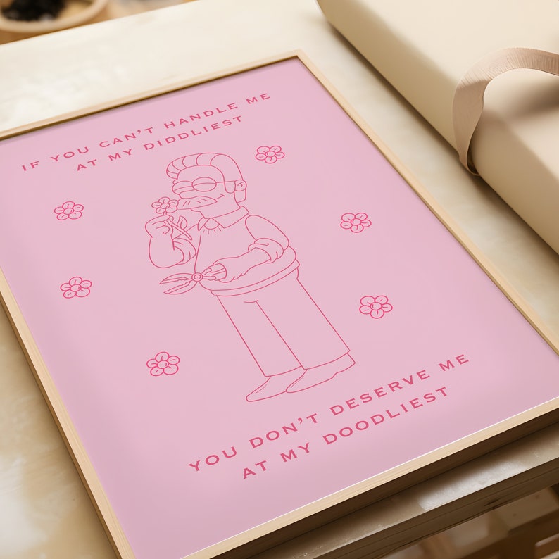 May include: A pink framed print with a cartoon illustration of a man with a mustache and glasses holding a pair of gardening shears and smelling a flower. The text on the print reads "If you can't handle me at my diddliest, you don't deserve me at my doodliest."
