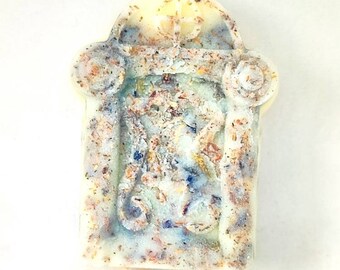 Könnte beinhalten: Eine weiße Seifenstange mit einem dekorativen Design, das ein blaues und goldenes Blumenmuster zeigt. Die Seife hat eine strukturierte Oberfläche und ist in Form eines kleinen Torbogens.