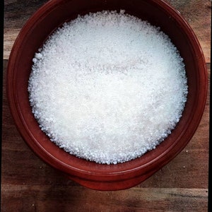 以下が含まれることがあります： 白い塩の結晶で満たされたテラコッタ製のボウルをクローズアップした写真です。