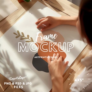 Op de afbeelding: Een witte frame mockup met een hand die het frame vasthoudt. Het frame staat op een houten oppervlak. Het frame heeft een verhouding van 4x5 inch. De tekst "Frame Mockup" staat in grote witte letters op het frame. De tekst "Artprintschool" staat in kleinere witte letters op het frame. De tekst "Smart Layer! PNG & PSD & JPG FILES" staat in kleinere witte letters op het frame.