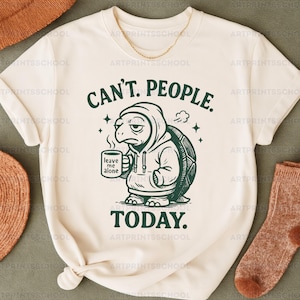 May include: Cream-colored t-shirt with a green illustration of a turtle wearing a hoodie and holding a mug. The text "CAN'T. PEOPLE. TODAY." is above and below the turtle. The mug reads "leave me alone."