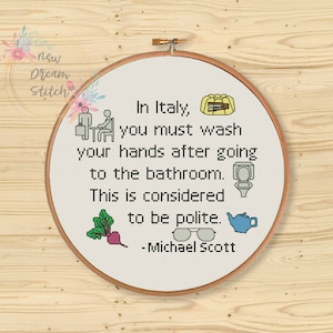 May include: A white cross-stitch embroidery hoop with a quote from the TV show "The Office" that reads: "In Italy, you must wash your hands after going to the bathroom. This is considered to be polite. -Michael Scott". The embroidery includes small colorful icons.